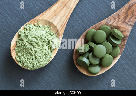 Chlorella tablets and young green barley powder on two wooden spoons on a dark background Stock Photo