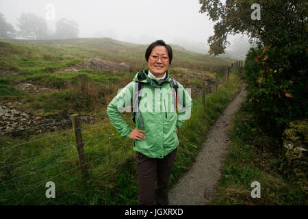 Smiling East Asian, misty morning,  Woman hiking in Lake District, Cumbria, UK. Stock Photo