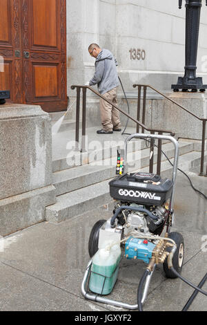 Building maintenance man cleaning building entrance with pressure washer machine - USA Stock Photo