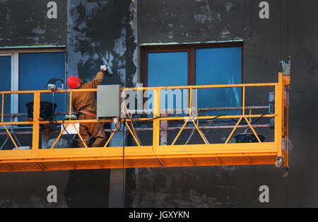 The gondola lift or scaffold with the worker on the building construction site. workers plastered the wall of the building Stock Photo