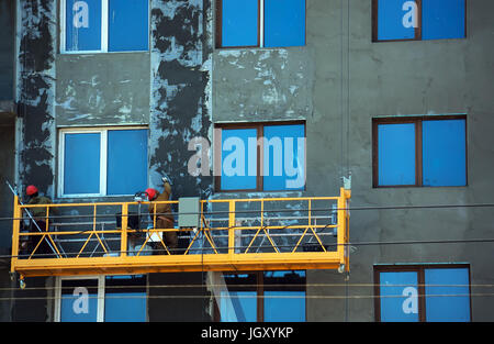 orange construction Elevator with the workers against the wall of a building under construction. Rachie make the facade of the building Stock Photo
