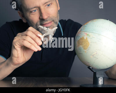 Handsome man looking a small globe to find the next travel destination Stock Photo