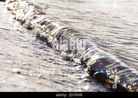 A small wave crashes on the beach in metallic morning light. Stock Photo