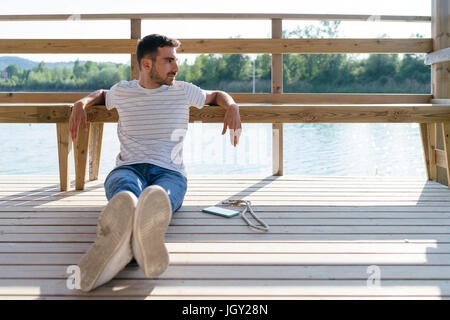 Man relaxing on pier, smartphone beside him Stock Photo