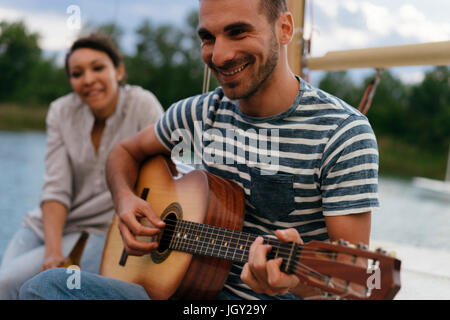 Man and woman relaxing on moored sailing boat, man playing guitar Stock Photo