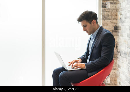 Businessman sitting on office chair typing on laptop Stock Photo