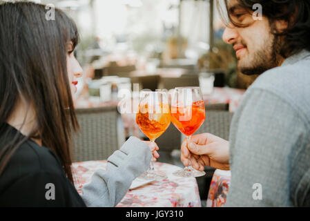 Young couple sitting outside cafe, holding drinks, making a toast Stock Photo