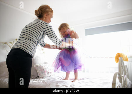 Young girl dressed in fairy costume, standing on bed, mother lifting her Stock Photo