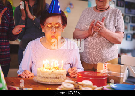 Senior woman blowing out candles on birthday cake at party Stock Photo