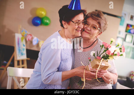 Senior woman giving flowers to friend at birthday party Stock Photo