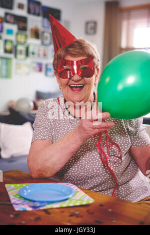 Senior woman waving balloons at birthday party Stock Photo