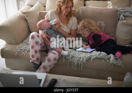 Mother feeding baby son and helping daughter with digital tablet Stock Photo