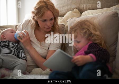 Mother feeding baby son and helping daughter with digital tablet Stock Photo