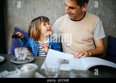 Girl playing with father's sunglasses in cafe Stock Photo