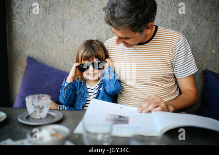 Girl playing with father's sunglasses in cafe Stock Photo