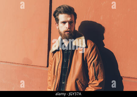 Portrait of cool young bearded man leaning against orange wall Stock Photo