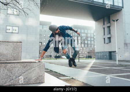 Young male hipster jumping mid air practicing parkour in city Stock Photo