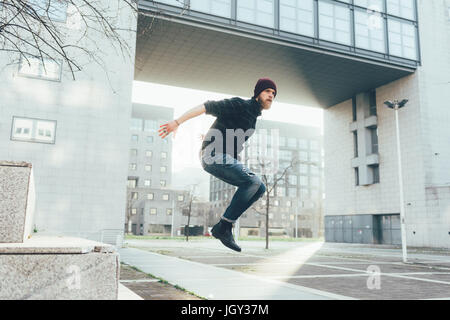 Young male hipster jumping mid air practicing parkour in city Stock Photo