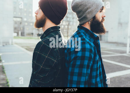 Portrait of two young male hipsters in knit hats back to back in city Stock Photo