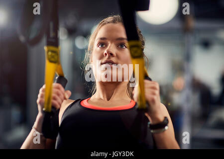 Young woman doing pull ups on exercise handles in gym Stock Photo
