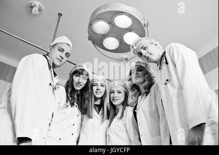 Confident and talented surgeons gathered around surgical light in the operating room. Black and white photo. Stock Photo