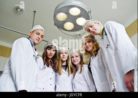 Confident and talented surgeons gathered around surgical light in the operating room. Stock Photo