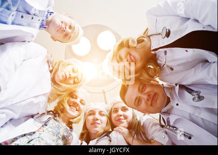 Confident and talented surgeons gathered around surgical light in the operating room. Stock Photo