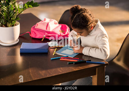 Adorable little girl sitting at table and drawing with colorful felt tip pens, doing homework concept Stock Photo
