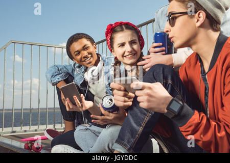 teenagers having fun with smartphones in skateboard park, hipster students concept Stock Photo