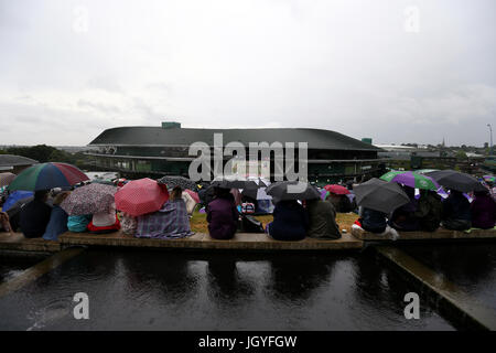 Spectators shelter from the rain under umbrellas as they watch Johanna Konta against Simona Halep on the big screen on Murray Mound on day eight of the Wimbledon Championships at The All England Lawn Tennis and Croquet Club, Wimbledon. Stock Photo