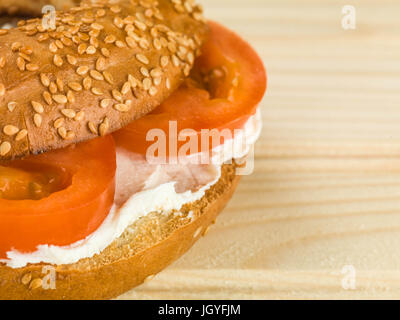 Cheese and Tomato Sesame Seed Bagel Against a Light Wooden Background Stock Photo