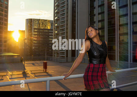 Black woman at sunset, stands leaning on the grill. Urban and architectural background, city view. Stock Photo