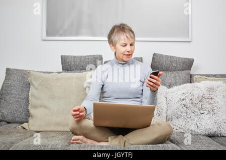 Modern senior woman on her couch using smartphone Stock Photo