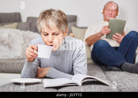 Senior woman drinking cup of coffee and reading book at home Stock Photo