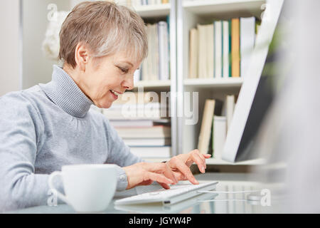 Senior woman writing and typing on keyboard from PC Stock Photo