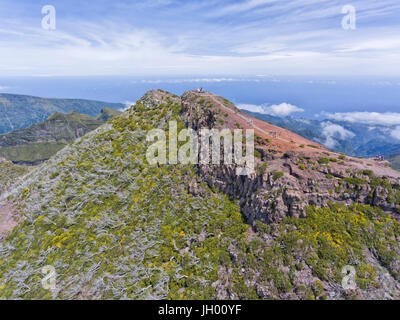 Aerial view of the highest mountain peak in Madeira island, Pico Ruivo, with walkers on a hiking trail to the top and clouds below in the valley . Stock Photo