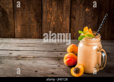 Homemade organic smoothie from yogurt and apricot. In Mason Jar, on a rustic old wooden table, with apricots and mint leaves. Copy space Stock Photo