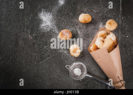 Homemade baking, puff pastries. Trendy food. Cronuts popcorn, puff donuts holes, in paper bag, with powdered sugar. On a dark stone table. Copy space  Stock Photo