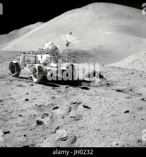 Roving Hills. David R. Scott, Commander of Apollo 15, works at the Lunar Roving Vehicle (LRV) during the third lunar surface extravehicular activity (EVA) of the mission at the Hadley-Apennine landing site. Hadley Rille is at the right center of the picture. Hadley Delta, in the background, rises approximately 4,000 meters (about 13,124 feet) above the plain. St. George Crater is partially visible at the upper right edge. This photograph was taken by Lunar Module pilot James B. Irwin. This view is looking almost due South.. Photographer: NASA Stock Photo
