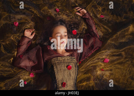 Portrait of cute young queen or princess laying on the ground covered with petals Stock Photo