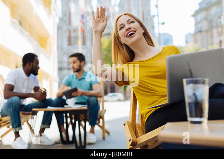 I am here. Stunning graceful positive lady holding her hand up while spotting her colleague whom she waiting on a terrace Stock Photo