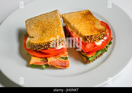 A BLT on a white dish, with bacon, lettuce, tomato, and mayonnaise on toasted wholewheat bread, a classic American sandwich Stock Photo