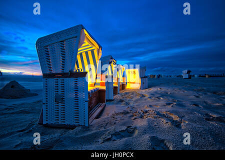 Twilight at the beach of Sank Peter Ording in north Germany. Beach chairs are gentle illuminated by lights during stormy sun set Stock Photo