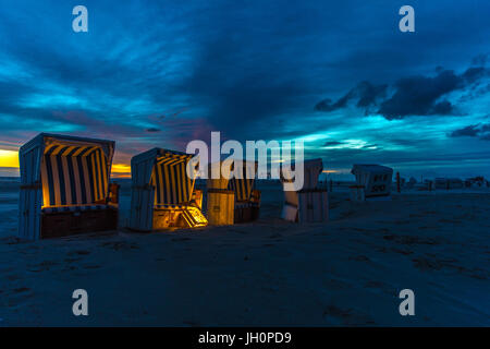 Twilight at the beach of Sank Peter Ording in north Germany. Beach chairs are gentle illuminated by lights during stormy sun set Stock Photo