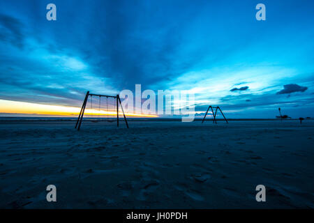 Twilight at the beach of Sank Peter Ording in north Germany. Swings are gentle moving during stormy sun set Stock Photo