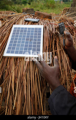 Brick factory worker using a solar panel to charge a cell phone battery. Uganda. Stock Photo