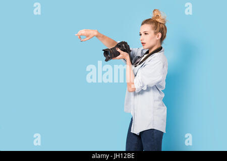 Woman blonde photographer shows how to pose to somebody. Model isolated on a blue background with copy space Stock Photo