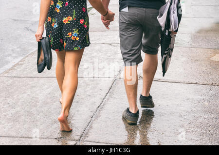 Couple on the street under the rain, woman walking barefoot Stock Photo