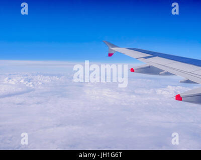 View from a plane window: a plane wing over clouds and blue sky. Traveling by air. Airplane flying above earth at 10000 m -50 Â°C  (-58.0 Â°F). Stock Photo