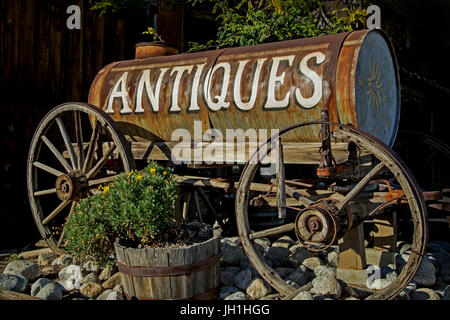 A sign for an antique store painted on the side of a broken down horse-drawn water tanker. Stock Photo